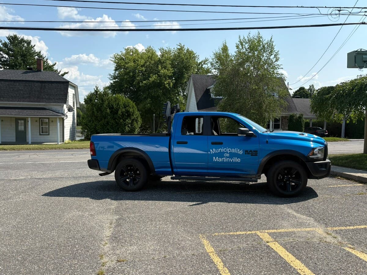 La camionnette RAM 1500 bleue de la Municipalité de Martinville, stationnée au village, des panneaux de signalisation dans sa boîte
