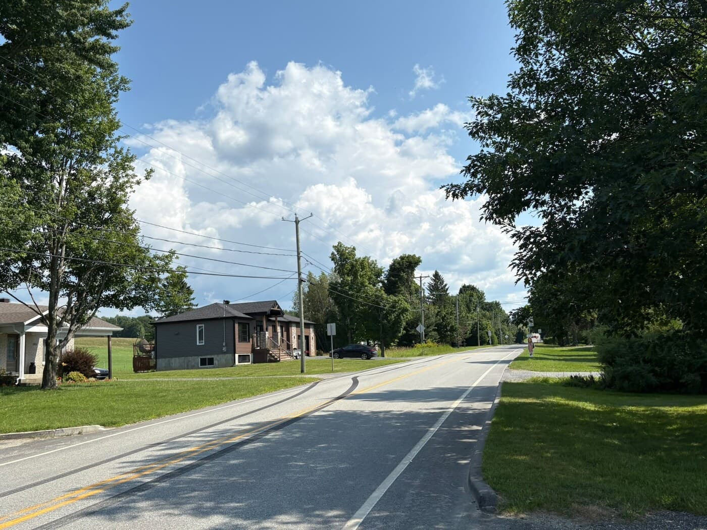 Rue résidentielle du village bordée de bungalows et de pelouses, sous de gros cumulus